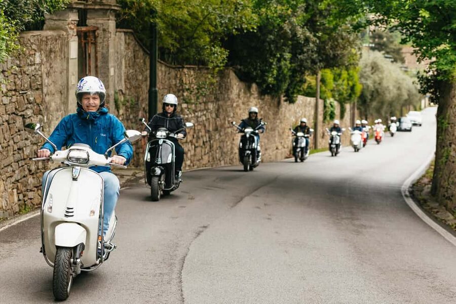 A line of Vespas on an open Italian road, riders in helmets